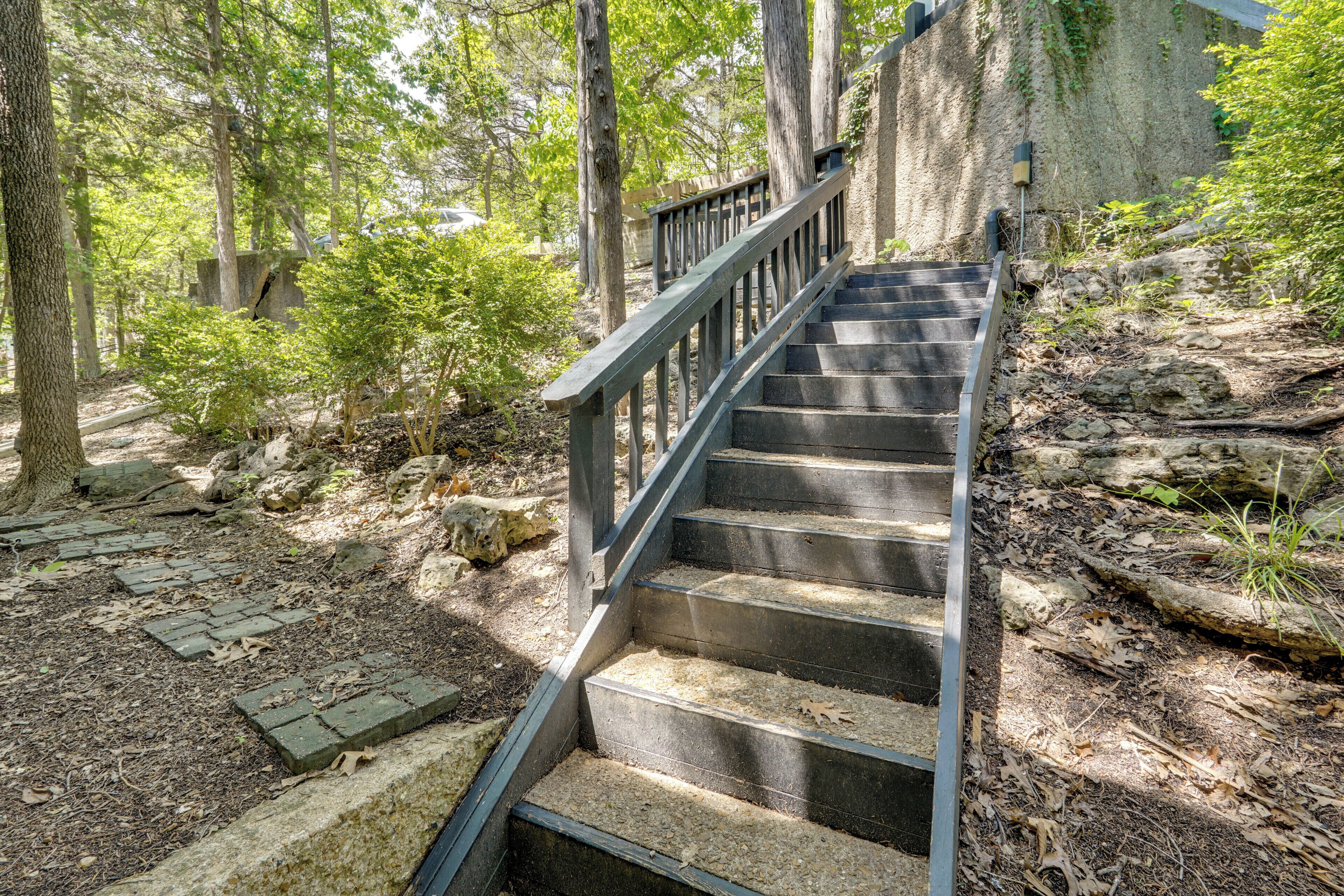 A wooden staircase leading up a stone wall, surrounded by trees and natural vegetation.
