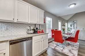 A modern kitchen with white cabinets, a dishwasher, and a dining area with red chairs.