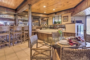 A rustic interior with wicker furniture, a glass-top dining table, and a bar area with shelves of glasses. - Montville Retreat Near Mohegan Sun: 2-home Bundle! (Montville)
