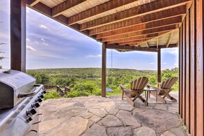 A covered outdoor area with a stone patio, a grill, and Adirondack chairs overlooking a forested landscape. - Montville Retreat Near Mohegan Sun: 2-home Bundle! (Montville)