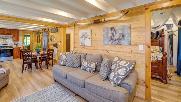 Un vaste espace de vie comprenant un canapé, une table à manger et des chaises, des poutres en bois au plafond et des œuvres d’art accrochées aux murs.
