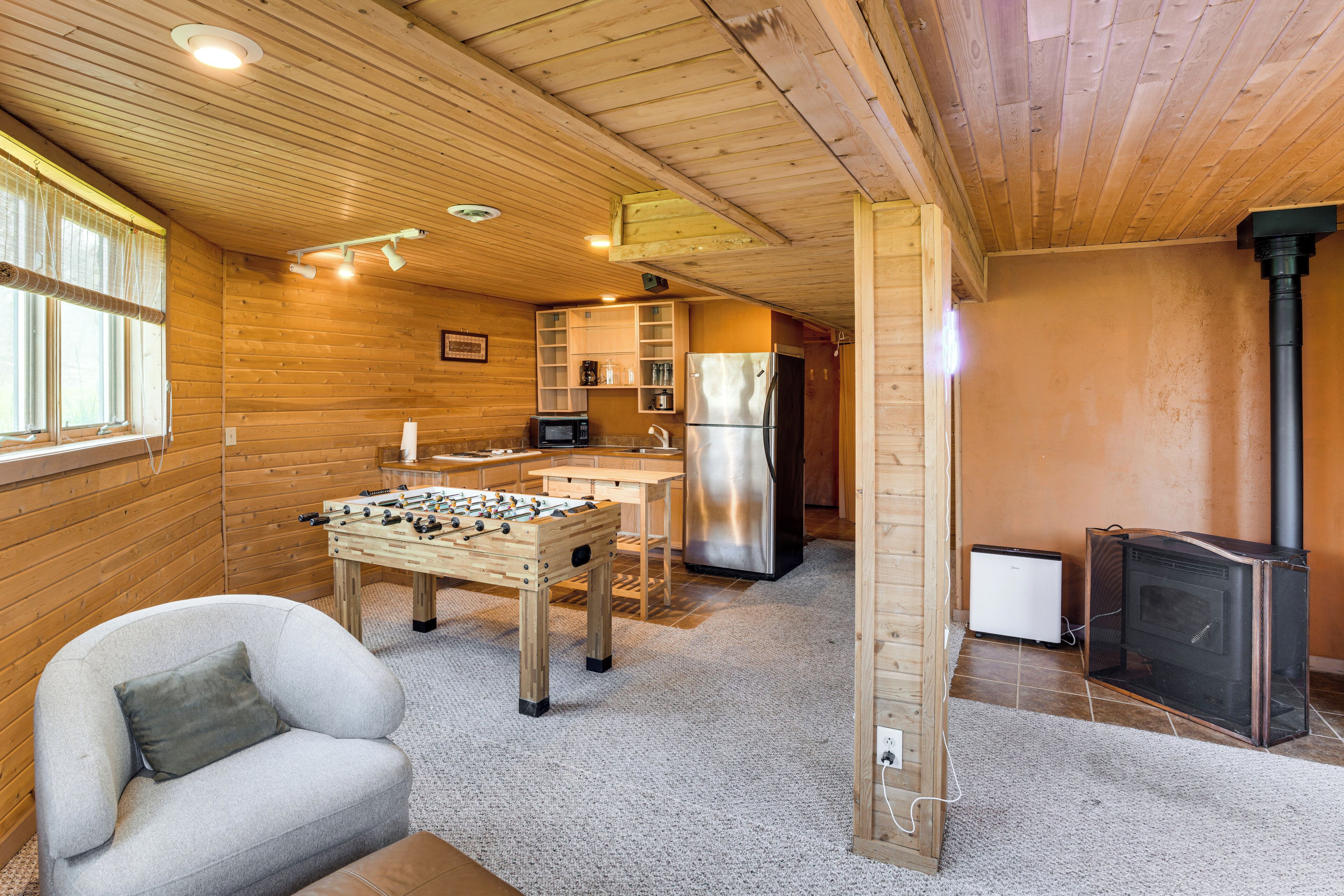 Um quarto aconchegante com mesa de futebol, sofá, cozinha equipada com frigorífico e lareira a lenha.