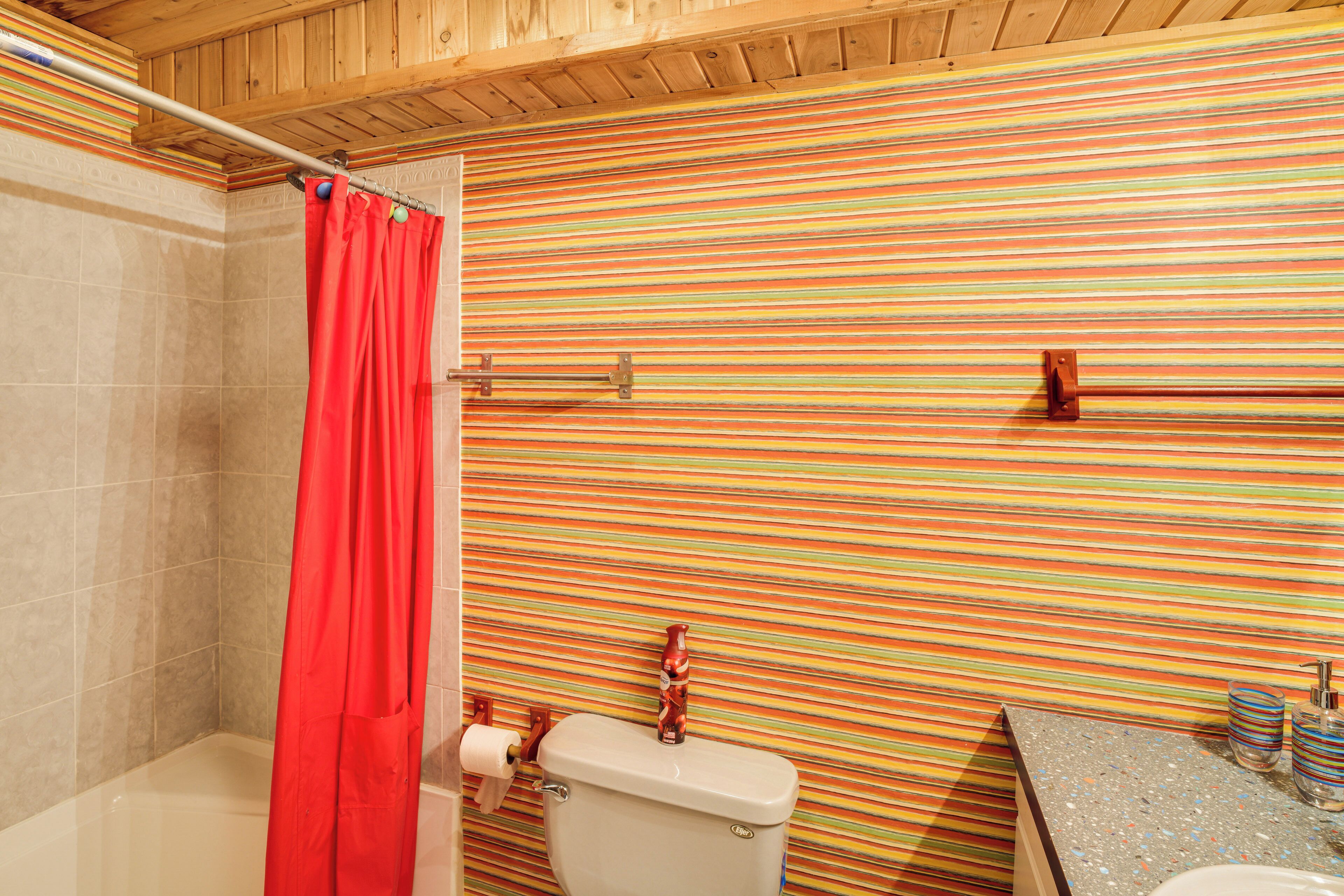 Een badkamer met een gestreepte wand, een douchegordijn, een toilet en een wastafel met gestreepte zeepdispensers.