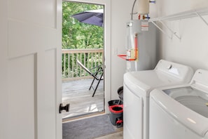Une buanderie équipée d’un lave-linge et d’un sèche-linge, une porte donnant sur un balcon et une petite poubelle.