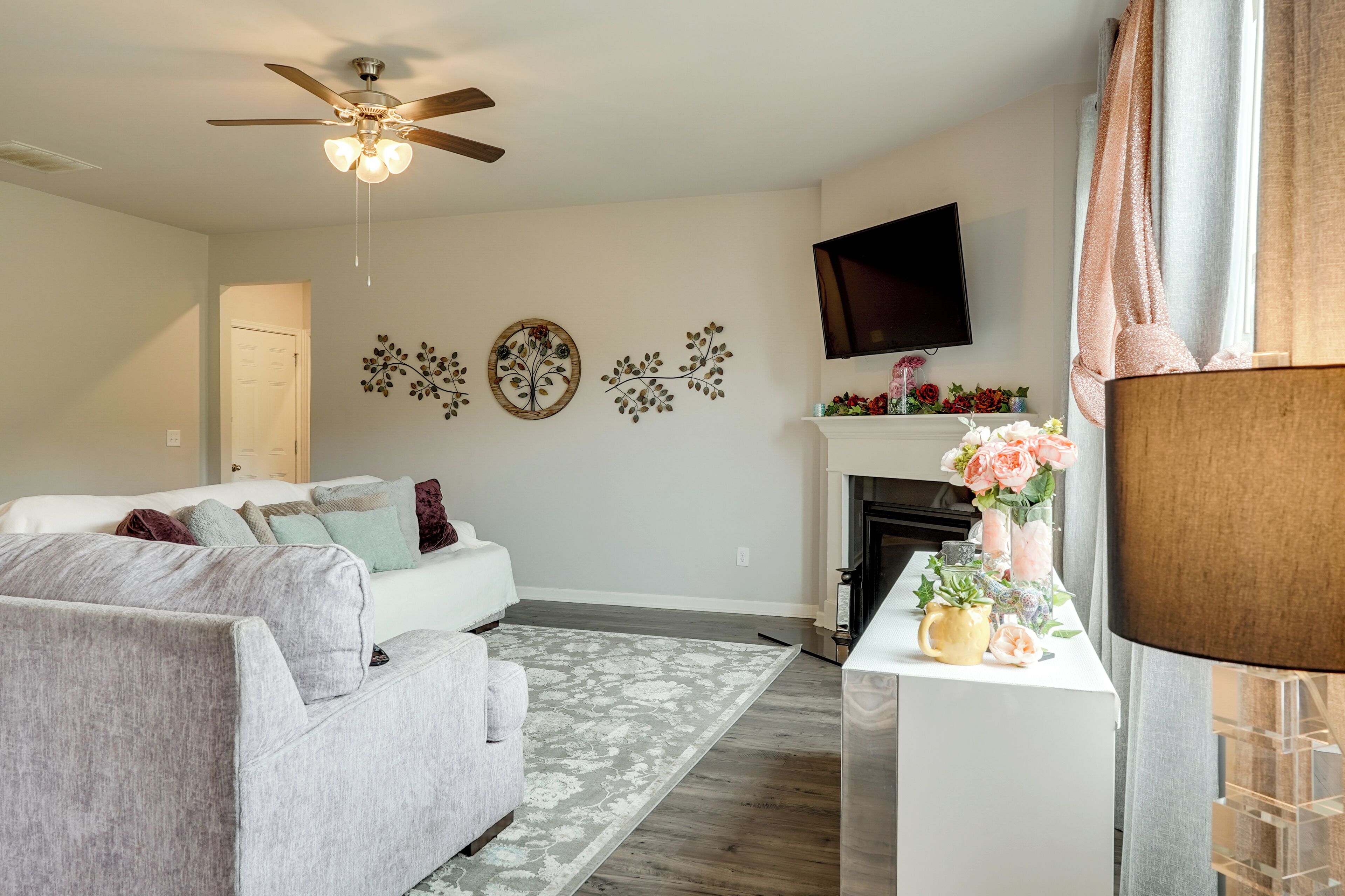 A living room with a grey sofa, a ceiling fan, a flat-screen TV, a fireplace, and decorative wall art.