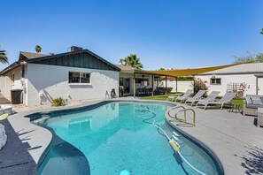 A swimming pool with a sunshade, lounge chairs, and a covered patio area.