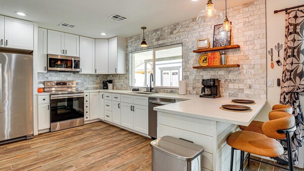 A modern kitchen with white cabinets, stainless steel appliances, a marble backsplash, and a bar area with stools. - Backyard Oasis! Group Retreat Near Tempe Town Lake (Tempe)