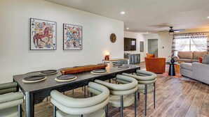 A dining area with a long table, bar stools, and a bar. There are two paintings on the wall, a clock, and a ceiling fan. - Backyard Oasis! Group Retreat Near Tempe Town Lake (Tempe)