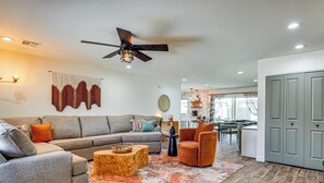 A living room with a sectional sofa, a coffee table, a chair, a ceiling fan, and a kitchen area in the background. - Backyard Oasis! Group Retreat Near Tempe Town Lake (Tempe)