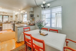 A kitchen with a dining table, chairs, a chandelier, and a window with blinds.