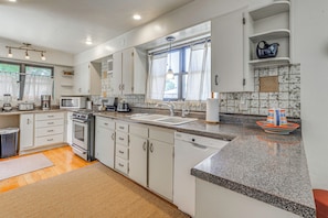 A modern kitchen with white cabinets, a granite countertop, a dishwasher, and a window with curtains. - Highly Walkable Area! Charming Roswell Bungalow (Roswell)