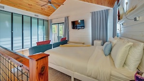 A bedroom with a large bed, a ceiling fan, a mounted TV, and a view of the outdoors through large windows. - Fishing Dock & Mtn Views! Buchanan Lake Family Gem (Burnet)