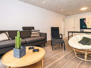 Una sala moderna con un sofá gris, una silla negra, una mesa de centro redonda de madera y una silla blanca de ratán.