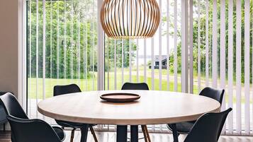 Una mesa de comedor redonda con seis sillas, una lámpara colgante y vistas a un paisaje verde a través de amplios ventanales.