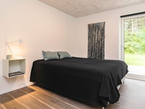 A bedroom with a bed, a bedside table with a lamp, and a view of greenery through a window. - 5 Star Holiday Home in Skals (Skals)