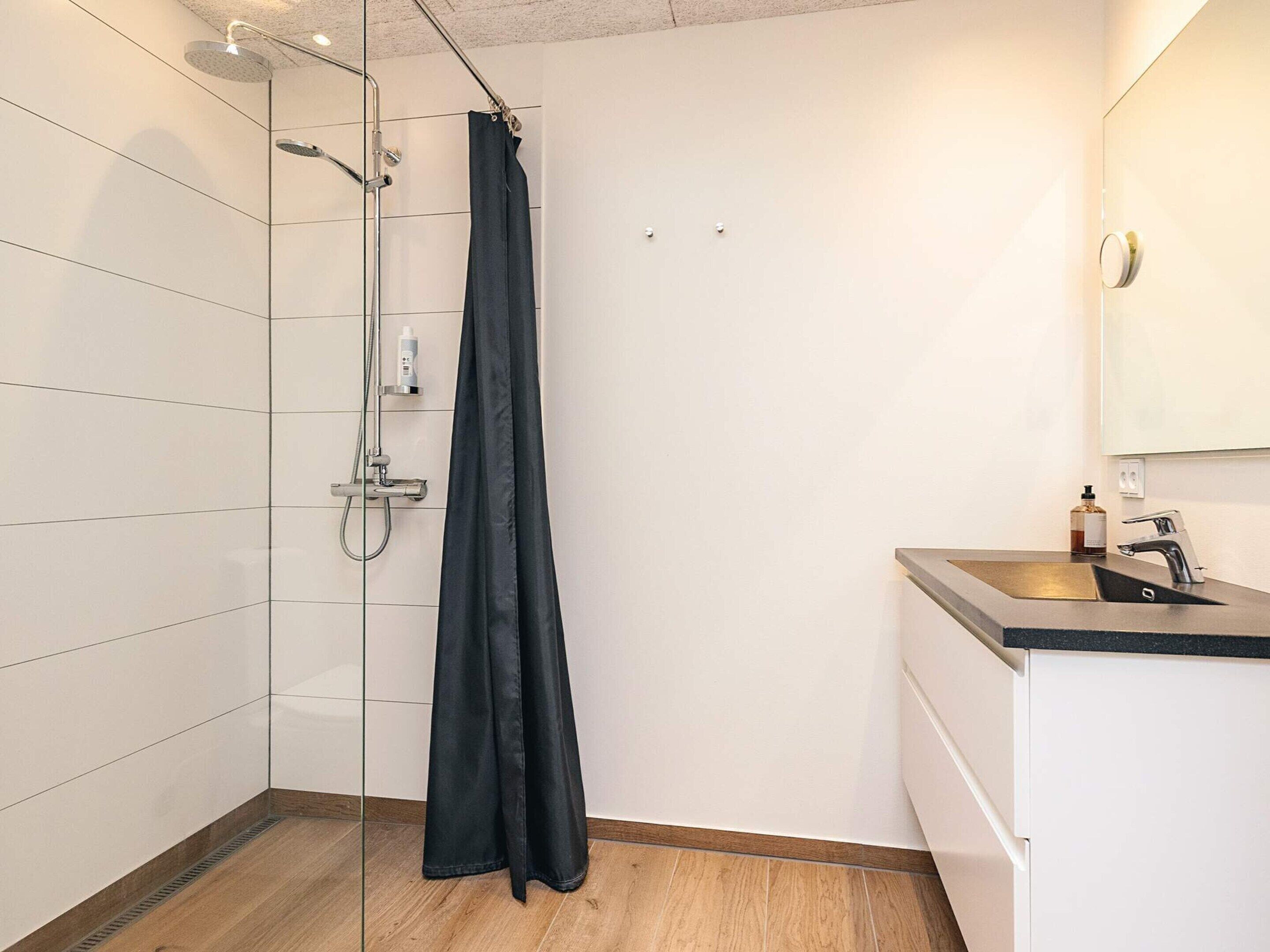 Een moderne badkamer met een douchecabine van glas, een wastafel met spiegel en een houten vloer.
