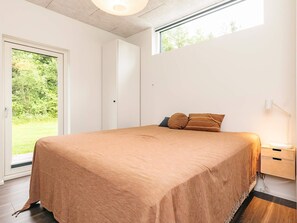 Un dormitorio con cama, mesita de noche, lámpara y puerta corredera que da a un jardín.