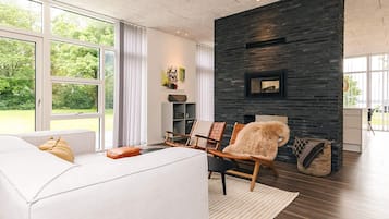 Una sala moderna con un sofá blanco, una chimenea y un ventanal grande.