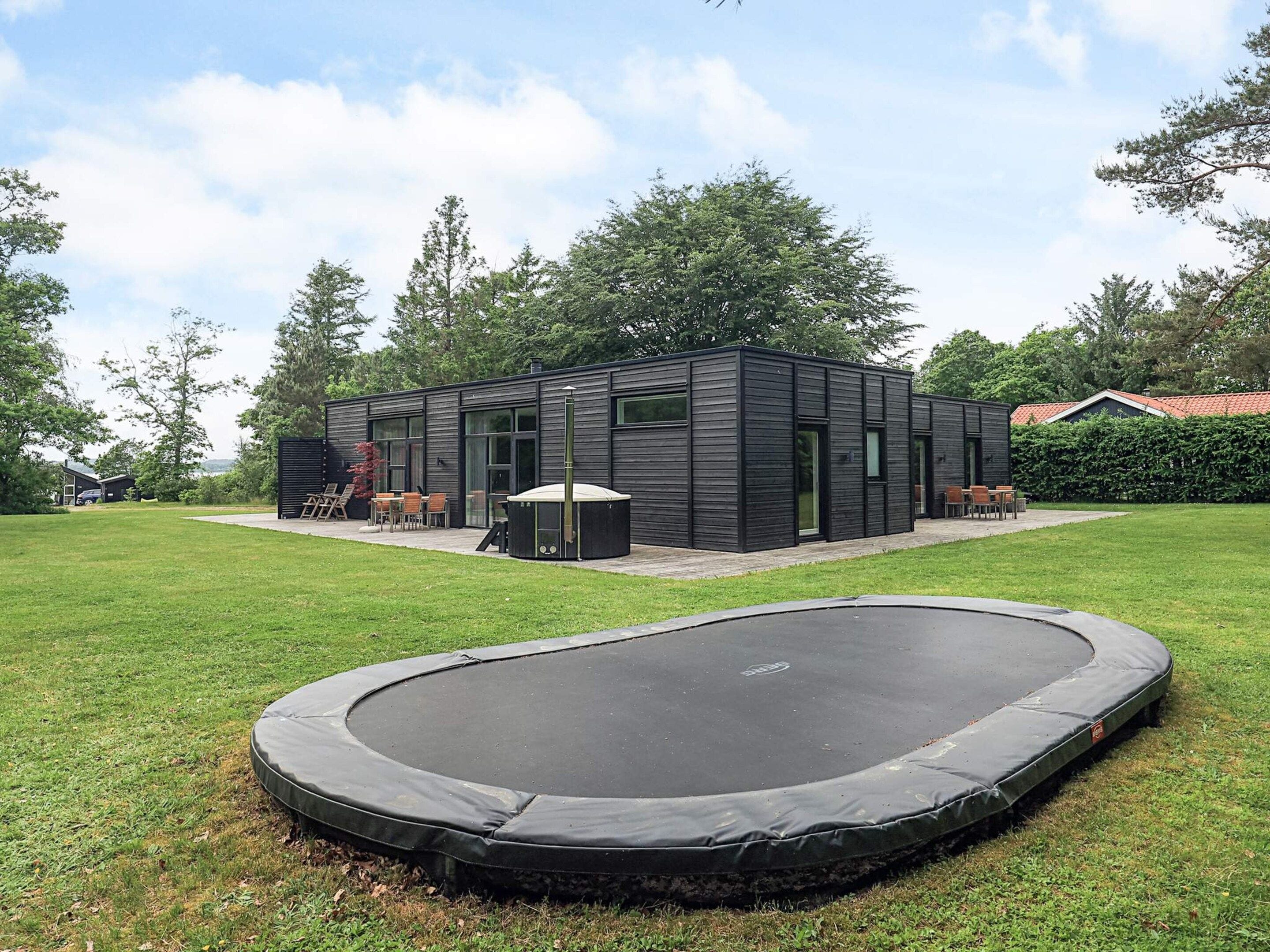 A modern house with a patio area, a trampoline, and a view of the surrounding greenery.