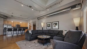 Una sala moderna con un sofá modular, una mesita de centro y una cocina al fondo.