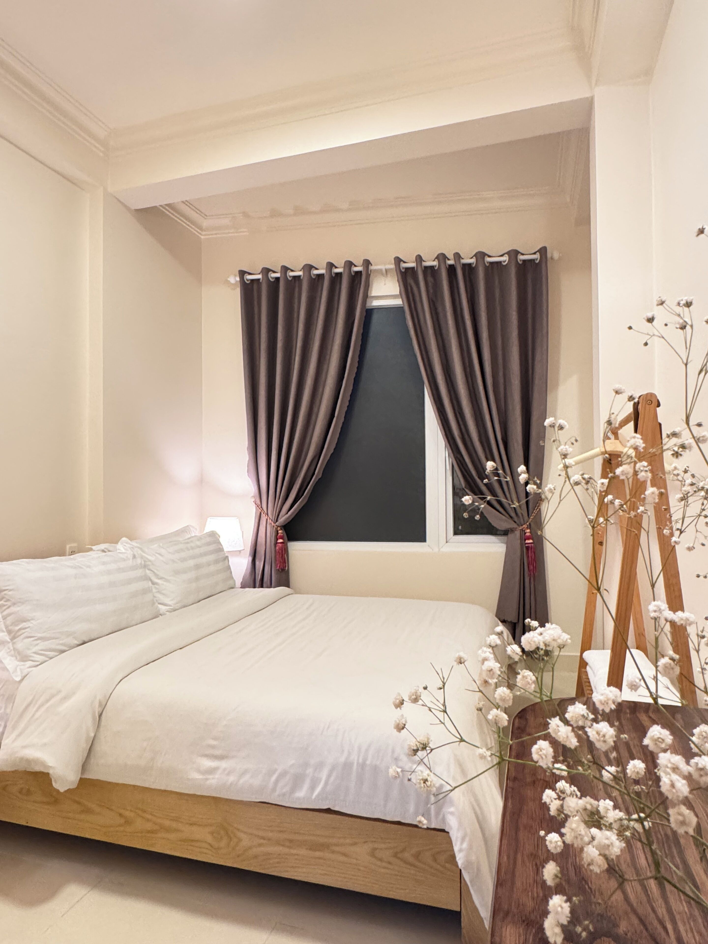 A bedroom with a bed, curtains, a window, and a vase with flowers.