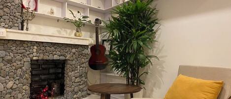 A cozy living room with a stone fireplace, a guitar, a potted plant, and a yellow cushion on a sofa.