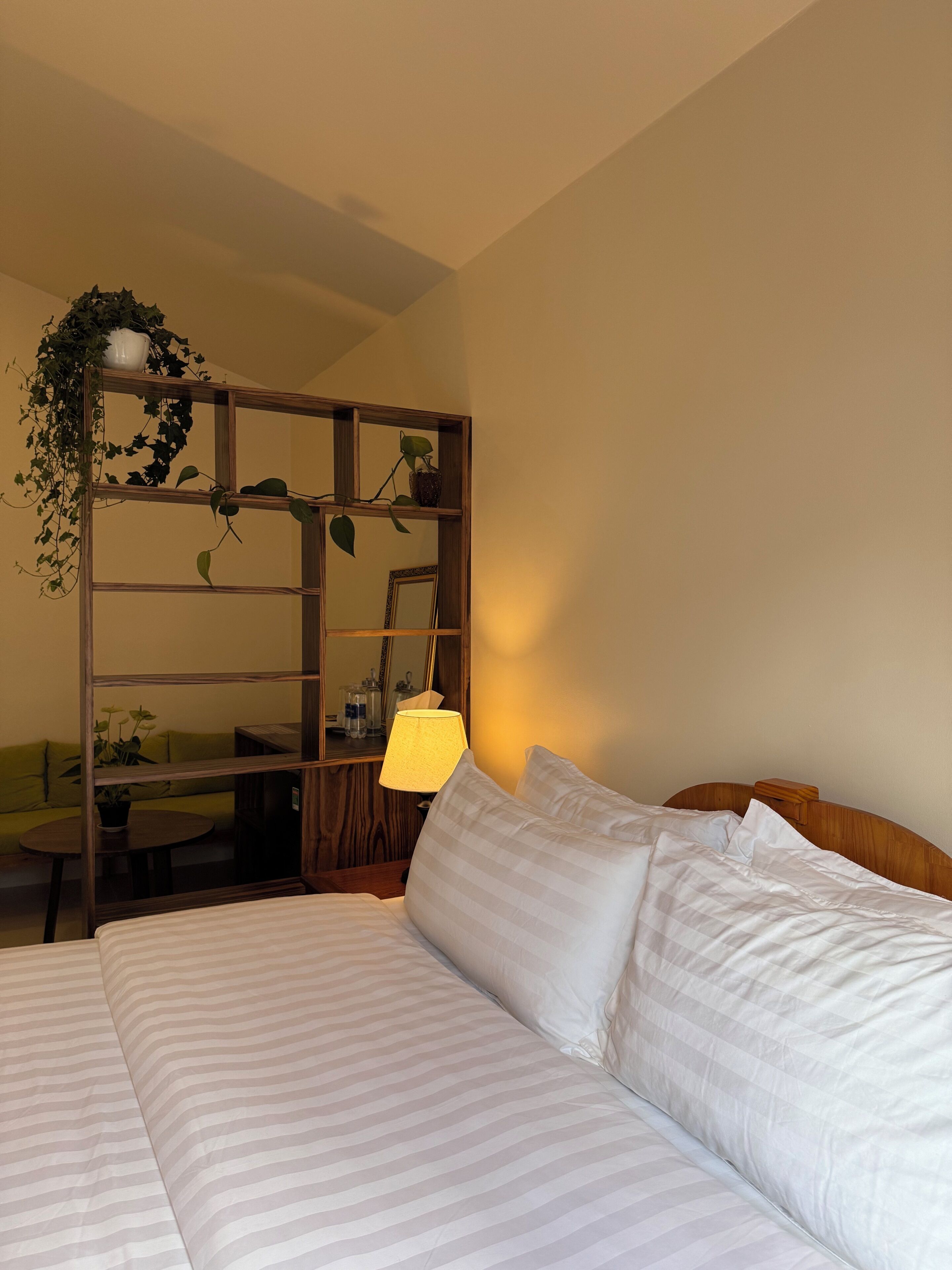 Et hotelværelse med seng, et træsidebord, en lampe, et spejl og en grøn sofa.