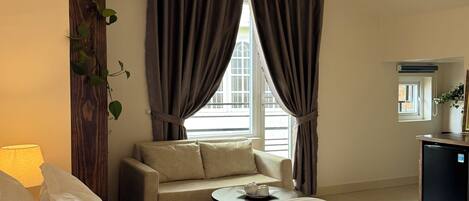 Ein Hotelzimmer mit Bett, einer Couch, einem kleinen Tisch mit Tablett, einem Schreibtisch und einem Fenster mit Vorhängen.