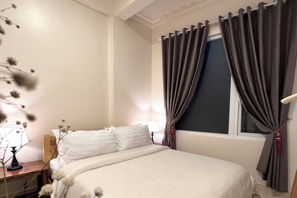 A bedroom with a bed, a nightstand, a lamp, and a window with curtains.