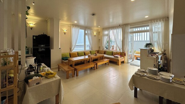 A living room with a sofa, tables, and a kitchen area with a refrigerator. - CozyNook Boutique Homestay (Xuan Huong - Da Lat)