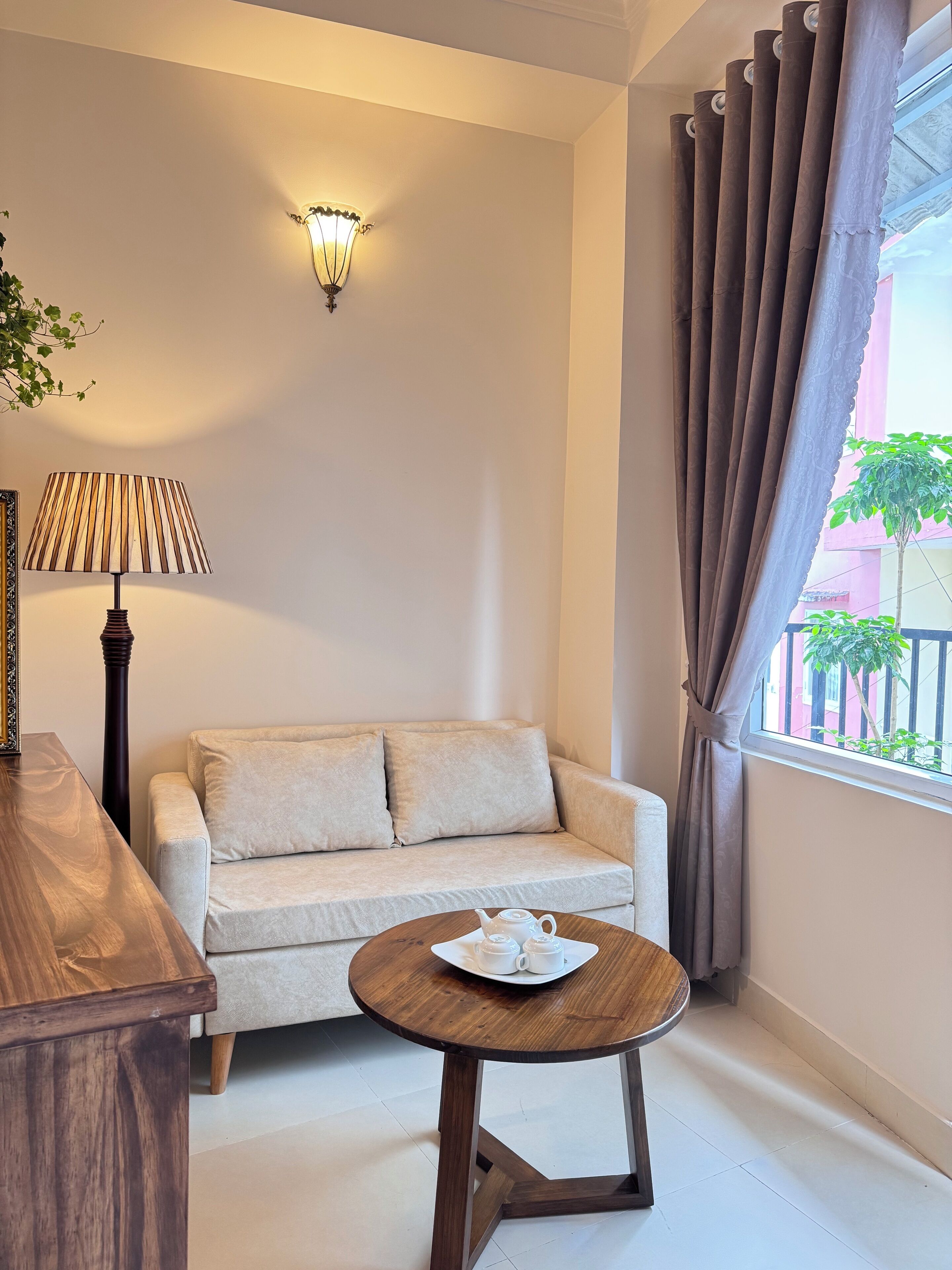A room with a sofa, a small round table with teacups, a lamp, and a wall-mounted light fixture.
