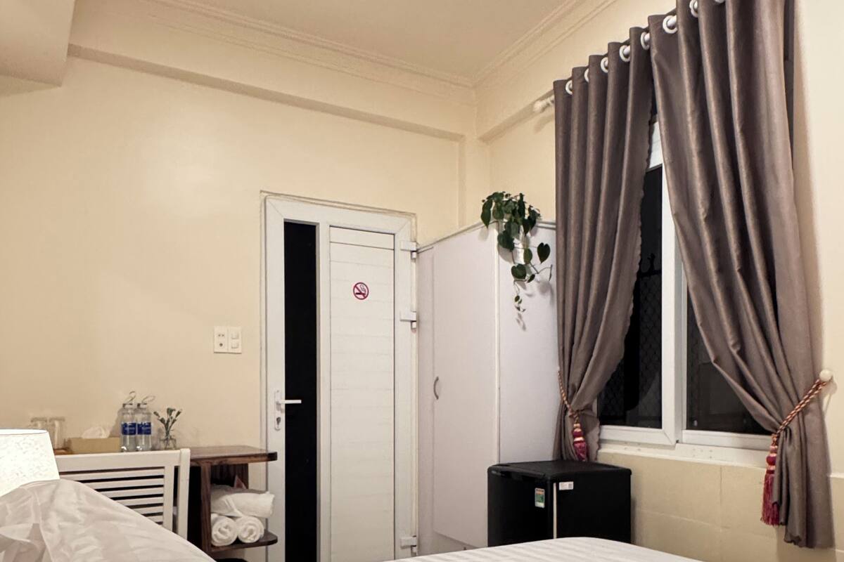 A hotel room with a bed, a desk with a computer, a radiator, a wardrobe, and a window with curtains.