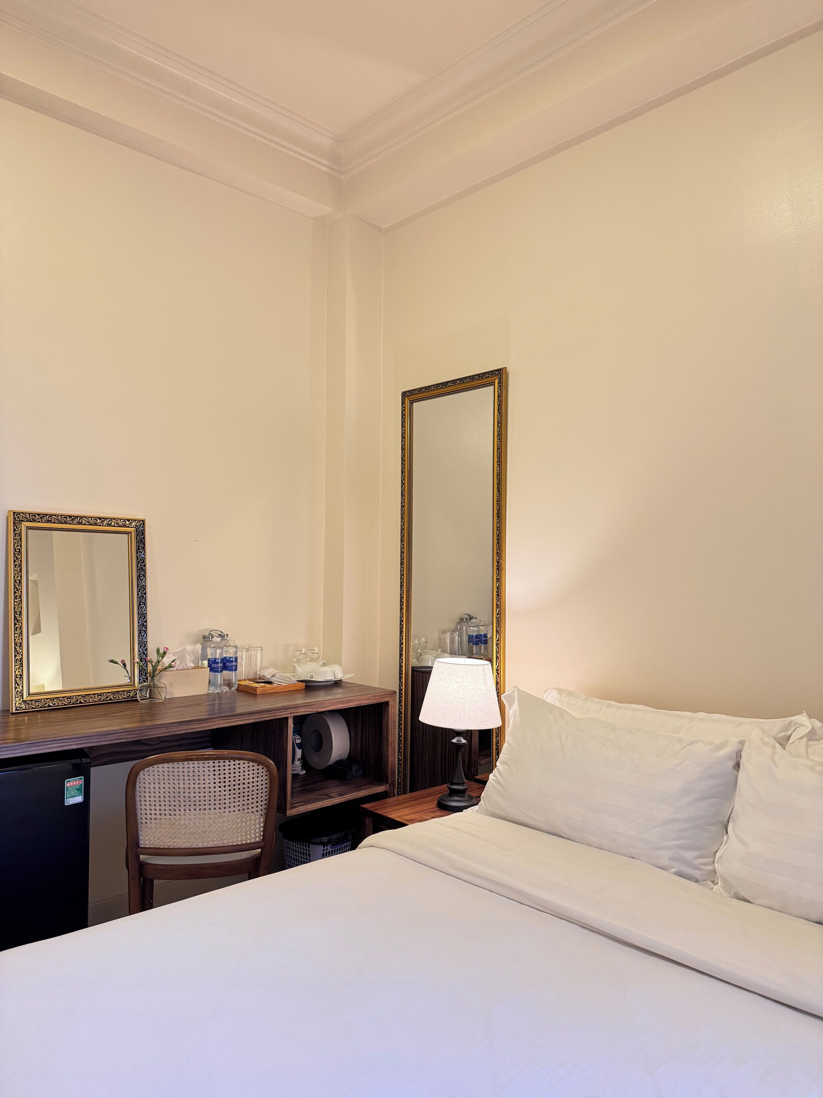 A hotel room with a bed, a desk with a mirror, a lamp, and a chair.