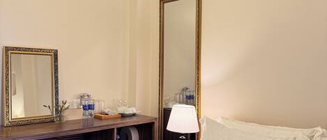 A hotel room with a bed, a desk with a mirror, a lamp, and a chair.