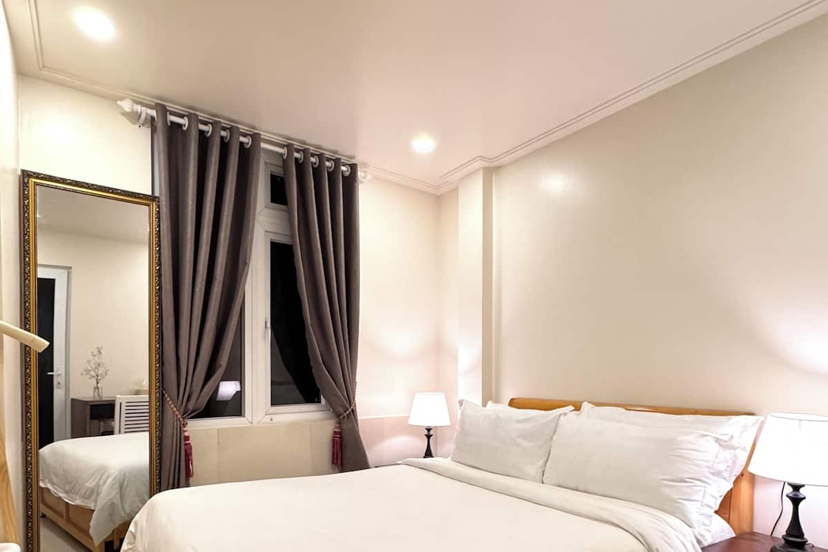 A hotel room with a large bed, a bedside table, a mirror, and a window with curtains.