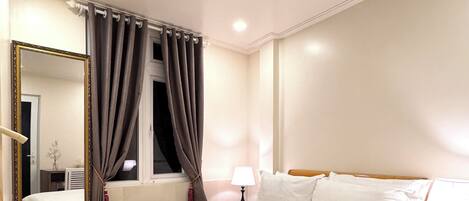 Une chambre d’hôtel avec un grand lit, une table de chevet, un miroir et une fenêtre avec des rideaux.