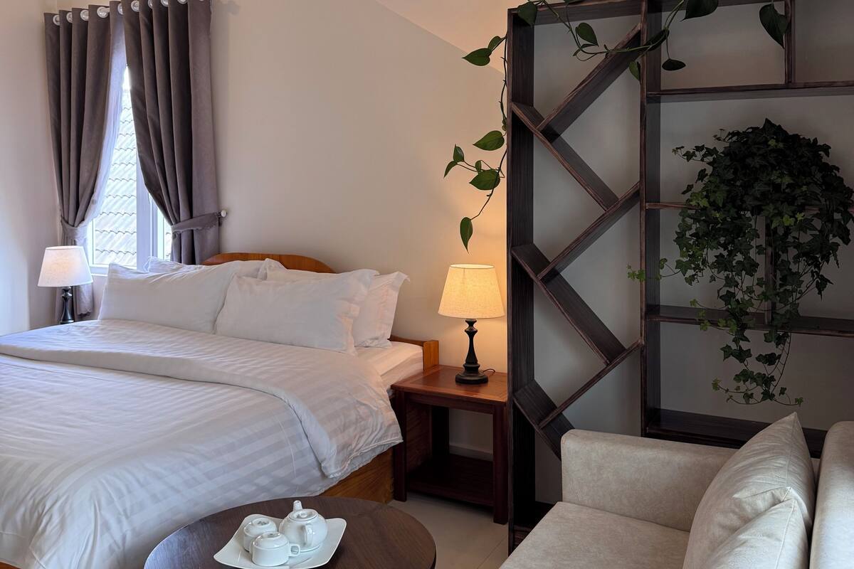 A hotel room with a bed, bedside table, lamp, and a sofa.