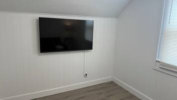 Une pièce dotée d’un téléviseur à écran plat fixé au mur, de murs recouverts de panneaux blancs et d’un plancher en bois.