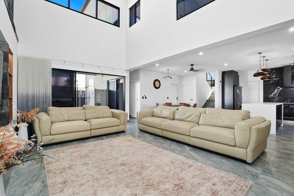 A spacious living area with two beige sofas, a large rug, and a kitchen in the background.