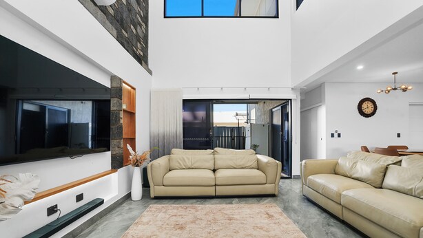 A modern living room with a large flat-screen TV, two beige sofas, a patterned rug, and a stone accent wall. - Ultra Modern Luxury Retreat with Pool in Northcrest Estate, sleeps 9 (Berrimah)