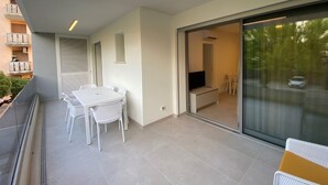 A balcony with a table and chairs, a sliding glass door leading to a room, and a view of a car on the street. - Cozy Apartment 300 m From the sea (San Michele al Tagliamento)
