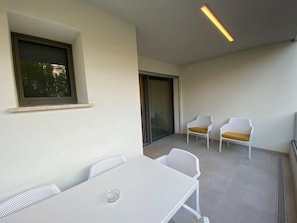 A balcony with a white table and chairs, a sliding glass door, and a ceiling light fixture. - Cozy Accommodation 300 m From the sea (San Michele al Tagliamento)