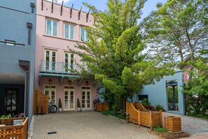 Un patio con un edificio rosa, una cerca de madera y un árbol.