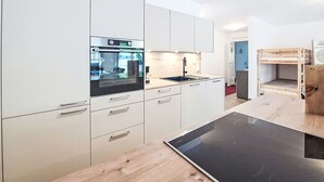Cozinha moderna com armários brancos, forno embutido, pia e mesa de madeira.