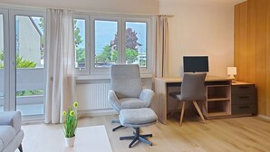 A modern room with a desk, two chairs, a potted plant, and large windows. - Cosy apartment for 4 people with WIFI, TV, balcony, pets allowed and panoramic view (Haag (rheintal))