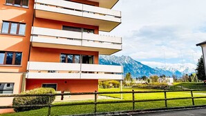 A multi-story building with balconies, a grassy area in front, and mountains in the background. - Cosy apartment for 4 people with WIFI, TV, balcony, pets allowed and panoramic view (Haag (rheintal))