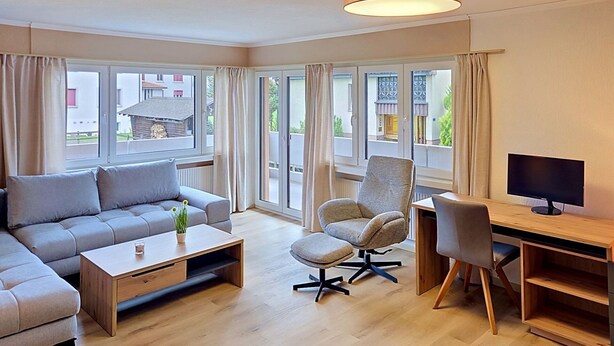 A modern living room with a sofa, armchair, coffee table, and a desk with a computer monitor. - Cosy apartment for 4 people with WIFI, TV, balcony, pets allowed and panoramic view (Haag (rheintal))