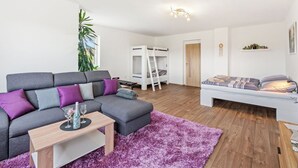 Ein modernes Wohnzimmer mit grauem Sofa, einem kleinen Tisch, einem violetten Teppich, einem Etagenbett und einem weißen Kleiderschrank.