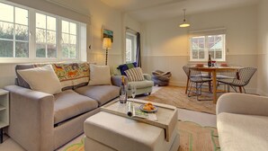 Ein Wohnzimmer mit Sofa, Hocker und einem Essbereich mit Tisch und Stühlen.