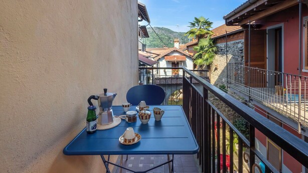 A balcony with a table set for breakfast, a chair, and a view of a village with buildings and a mountain. - Cosy apartment for 4 people with WIFI and balcony (Brovello)